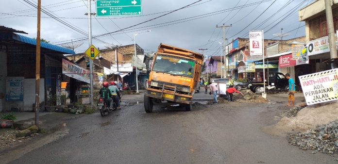 Akibat Jl Pdt Justin Sihombing rusak parah, satu truk bermuatan pasir dan batu nyaris terguling.