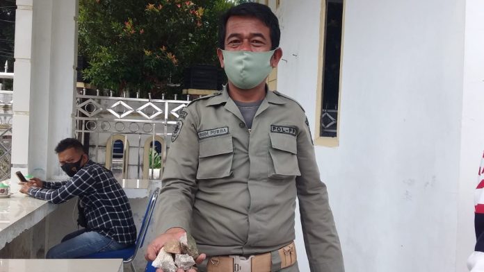 Anggota Satpol PP Siantar Budi Purba menunjukkan batu yang dilemparkan oknum diduga provokator di pos jaga gedung DPRD Siantar.  (f:mistar/billy nasution).
