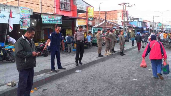 Personel Polsek Labuhan Ruku bersama Satpol PP membentuk pagar betis mencegah pedagang berjualan di badan jalan.