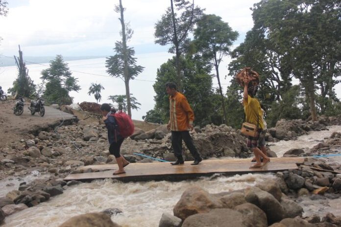 Warga berjalan diatas jembatan kayu dilokasi banjir di Nagori Purba Pasir, Kecamatan Haranggaol Horison.(f:indra/mistar)