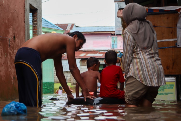 Seorang ayah menemani anaknya bermain banjir dengan ban