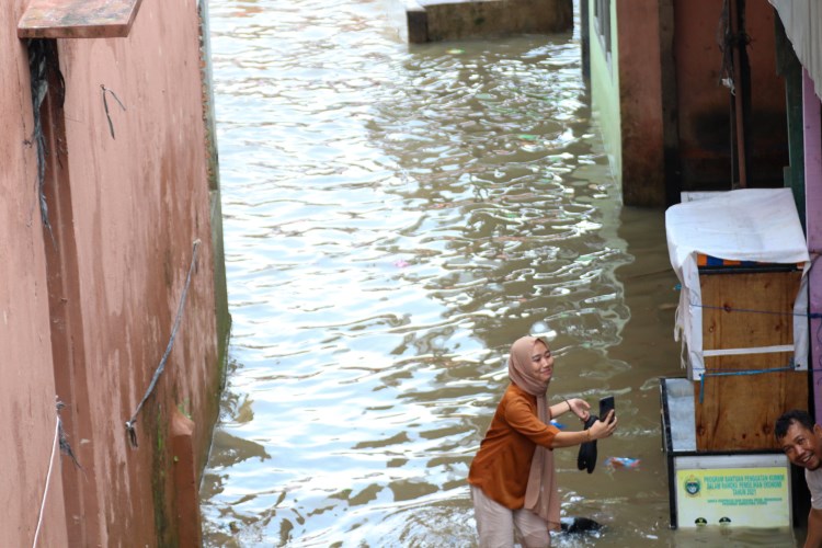Seorang perempuan tengah membuat konten di banjir Kampung Aur Kota Medan