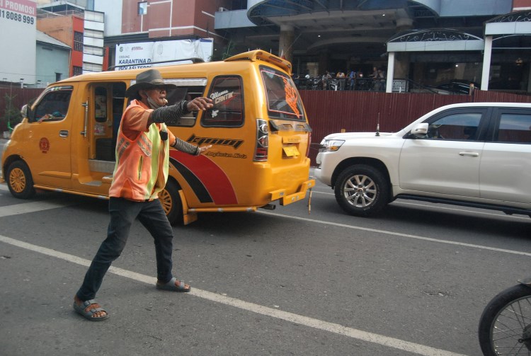 Seorang tukang parkir sedang mengatur kendaraan yang hendak parkir di Kota Medan