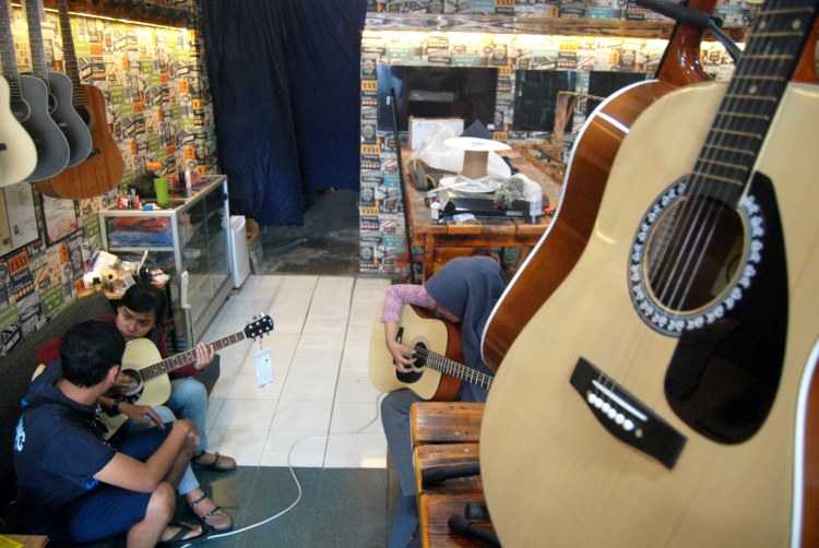Pekerja toko gitar di Medan tengah melayani pembeli