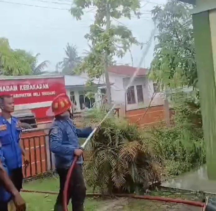 Pemadam berusaha memadamkan asap yang mengepul dari atas bangunan Posyandu Deli Serdang