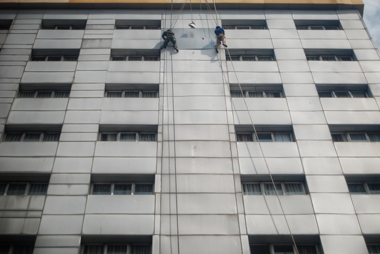 Dua orang pekerja tengah memperbaiki dinding luar gedung salah satu hotel di Kota Medan