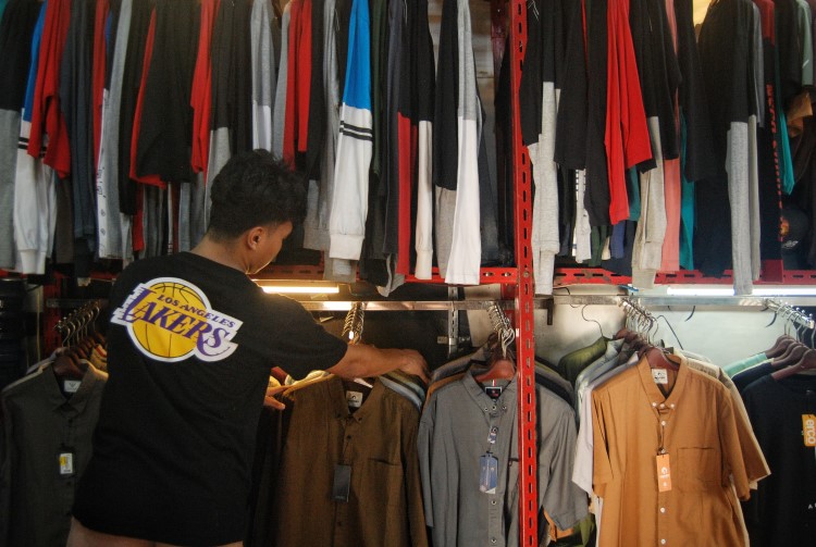 Pekerja toko pakaian di Medan merapikan baju yang tergantung