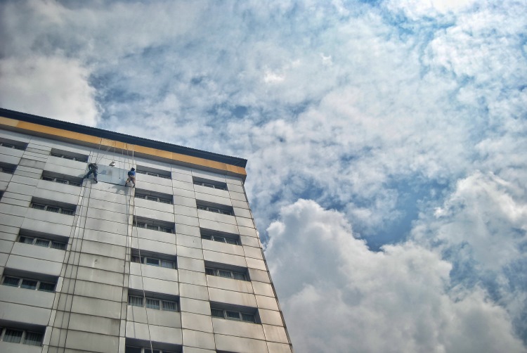 Sejumlah pekerja tengah bergelantungan sambil memperbaiki dinding luar gedung salah satu hotel di Kota Medan