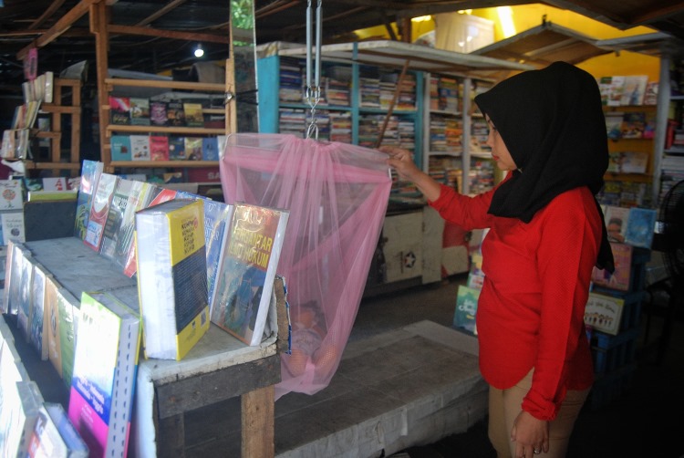 Siti Hasanah (44) mengayun anaknya sambil menunggu pembeli di toko buku miliknya di kawasan Titi Gantung, Medan, Sumatera Utara