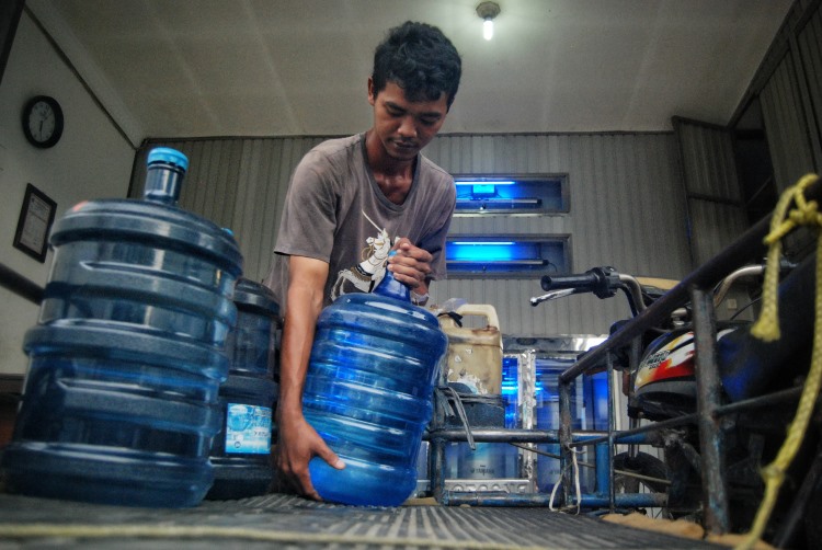 Pekerja depot air minum isi ulang di Medan mengangkat galon ke atas becak