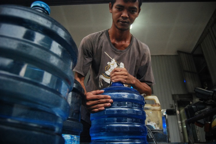 Pekerja depot air minum isi ulang sedang mengangkat galon milik pelanggan