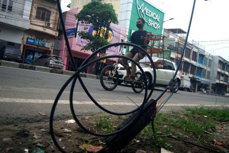 Pengendara melintas di depan kabel semrawut di Jalan HM. Yamin, Kota Medan