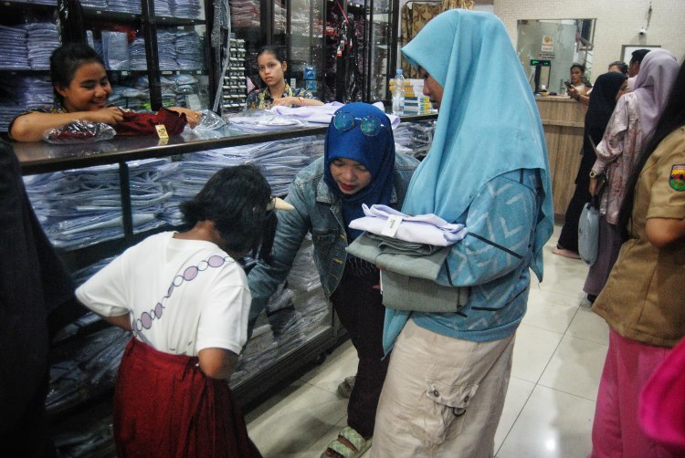 Seorang ibu mencoba memakaikan seragam sekolah kepada anaknya saat berbelanja di salah satu toko di Kota Medan