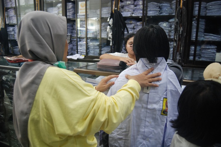 Seorang ibu menyocokkan ukuran seragam sekolah kepada anaknya saat berbelanja di salah satu toko di Kota Medan