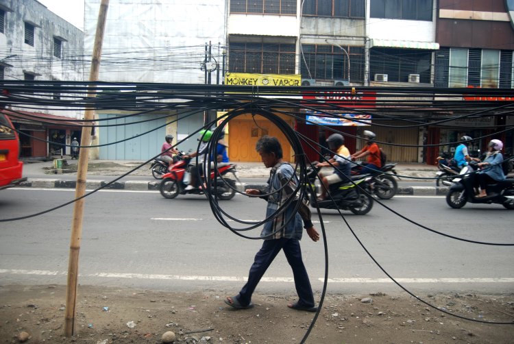 Seorang warga melintas di dekat kabel semrawut di Jalan HM. Yamin, Medan