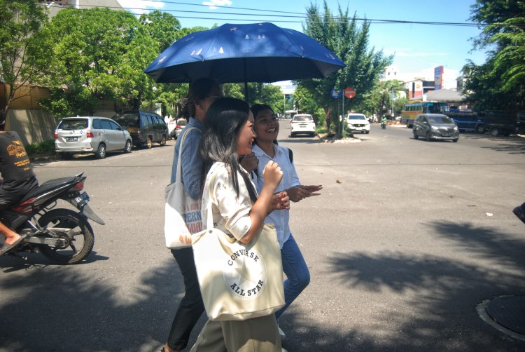 Warga menggunakan payung saat melintasi Jalan Sena, Kota Medan untuk menghindari sengatan cuaca panas