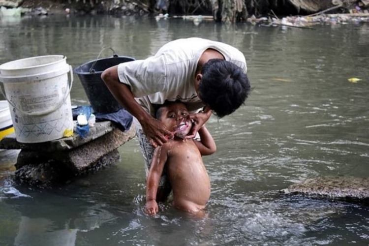 Warga yang tinggal di pinggiran aliran sungai Babura Kota Medan menyikat gigi anaknya menggunakan air sungai beberapa waktu lalu.