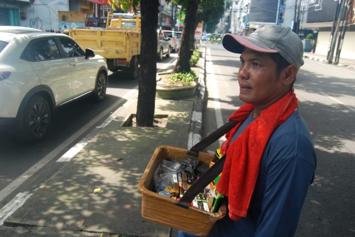 Doli (43) pedagang rokok asongan menjajakan dagangannya kepada pengguna jalan di persimpangan lampu merah Jalan Brigjen Katamso, Medan