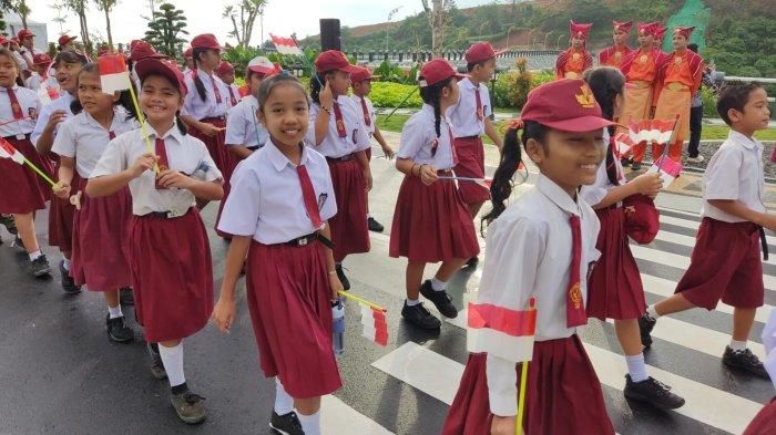 Pelajar SD berjalan dari sekolah berbaris rapi mengibarkan replika bendera merah putih menuju area area bendungan untuk melihat Presiden Jokowi.