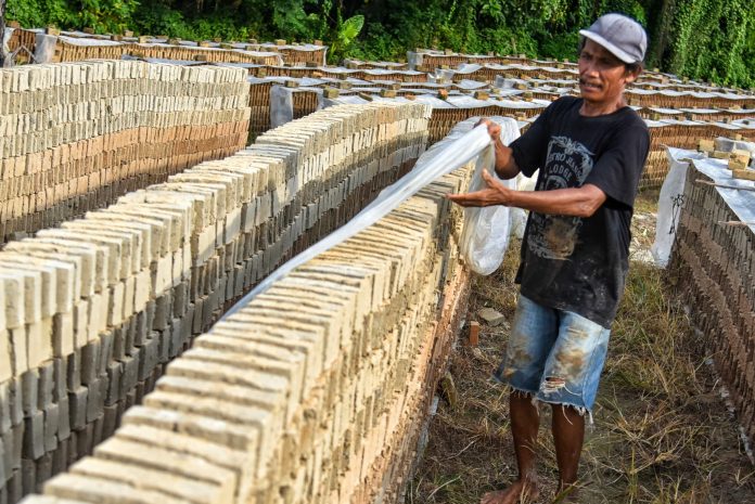 Perajin menutup batu bata yang dijemur menggunakan terpal di Pakam, Deli Serdang, Sumatera Utara