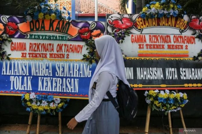 Seorang siswi melewati karangan bunga terkait kasus penembakan Siswa di Semarang.