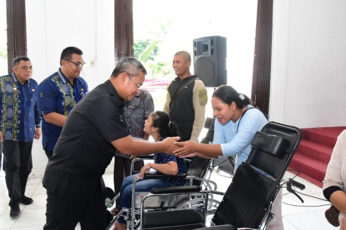 Pj Bupati Deli Serdang, Wiriya Alrahman didampingi Kadis Sosial, Rudi Akmal Tambunan menyerahkan bantuan kursi roda pada peringatan HKSN tahun 2024 di Balairung Pemkab Deli Serdang, Lubuk Pakam, Jumat (20/12/24). (f:rinaldi/mistar)